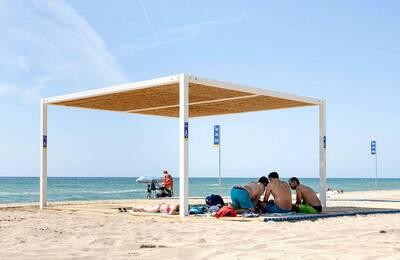 Gent a la platja disfrutant de l'ombra de la pergola