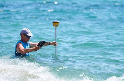 Un home pren mesures dins de l'aigua a tocar de la platja